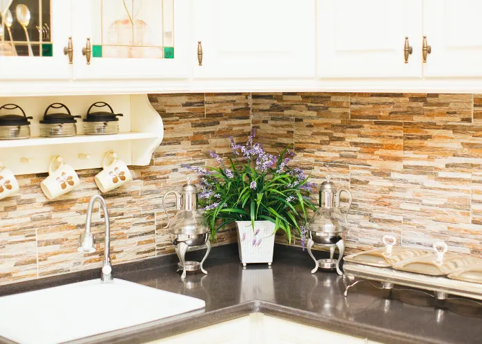 Beautiful light earth colored kitchen backsplash consisting of lighter and darker tan colors with a dark granite countertop